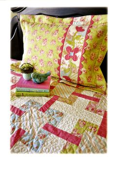 a bed topped with pillows and a quilt next to a book on top of it