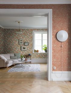 an open door leading to a living room with floral wallpaper and wood flooring