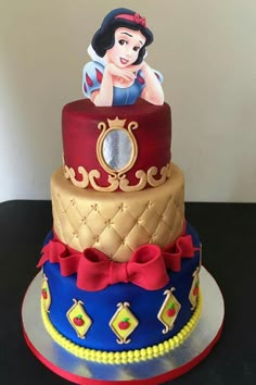 a three tiered cake with snow queen on top and red ribbon around the edges