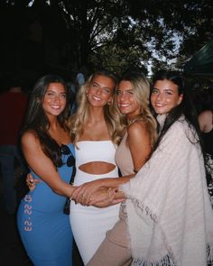 four beautiful young women standing next to each other at a party in front of a crowd