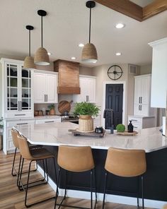 a large kitchen island with four stools in front of it and three lights hanging from the ceiling