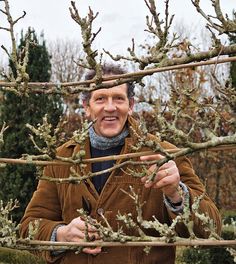 a man standing in front of a tree with no leaves on it and holding his hands up to the branches