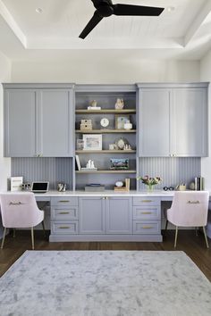 an office with gray cabinets and two pink chairs in front of a white ceiling fan