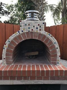 an outdoor brick pizza oven in the middle of a fenced area with palm trees