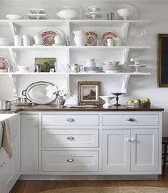 a white kitchen with open shelves and dishes on the top shelf in front of it