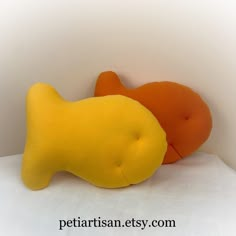 two yellow and orange stuffed animals laying next to each other on a white sheeted surface