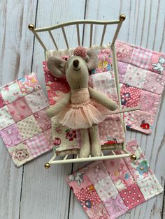 a stuffed animal in a pink dress sitting on top of a quilted patchwork blanket