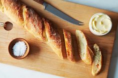 bread and butter on a cutting board next to a knife, spoons and salt