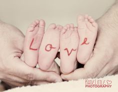 two hands holding three baby feet with the word love written on their fingers in red ink