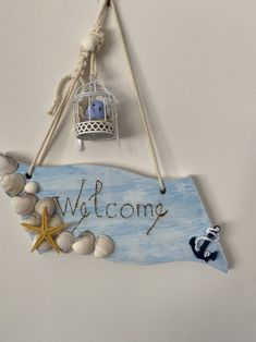 a welcome sign hanging from the side of a wall with seashells and starfish