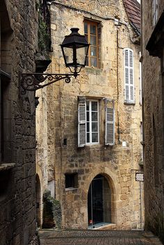 an old stone building with white shutters and a lamp on the street in front of it