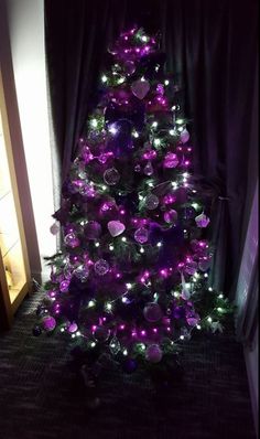 a purple christmas tree is lit up in the dark