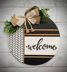 a welcome sign with a bow on it and greenery in the center, hanging on a white wooden wall