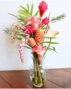 a vase filled with flowers and greenery on top of a wooden table next to a wall