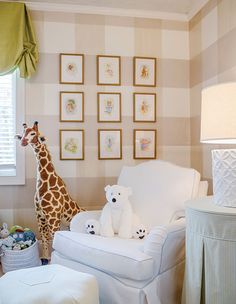 a giraffe standing next to a white chair in a room with pictures on the wall