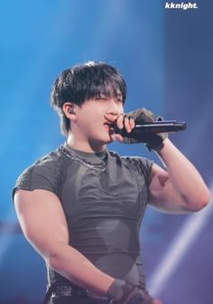 a male in a black shirt is holding a microphone up to his mouth and wearing gloves