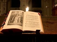 an open book sitting on top of a wooden table next to a lit candle in a church