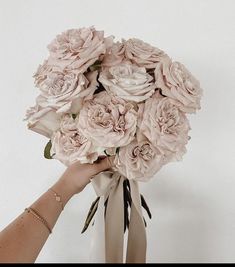 a bouquet of pink flowers being held by a woman's hand in front of a white wall