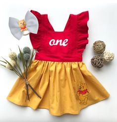 a red and yellow winnie the pooh dress next to some pine cones