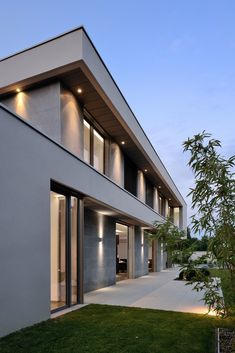 an exterior view of a modern house with grass in the foreground and lights on