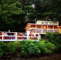 people are standing on the deck of a blue oak restaurant near some trees and water