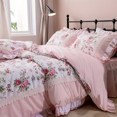 a bed with pink comforters and pillows in a room next to a large window