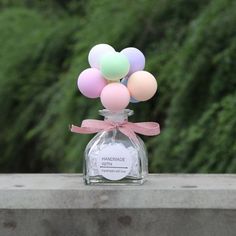 a bottle filled with pastel balloons on top of a cement wall next to trees