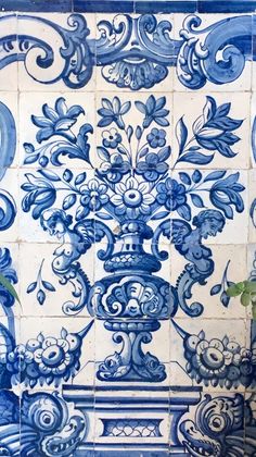 a blue and white tile wall with an ornate design on it's side, next to a potted plant