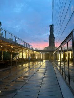 an empty walkway in front of a tall building at dusk with the sun setting behind it