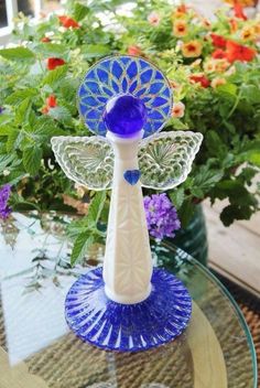 a glass table topped with a blue and white flower vase next to a plant filled with flowers