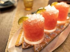 three glasses filled with drinks sitting on top of a wooden tray