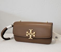 Eleanor leather crossbody bag from TORY BURCH featuring camel brown, calf leather, gold-tone logo plaque, gold-tone hardware, partitioned compartment, internal zip pocket, clip-lock fastening and single shoulder strap. Dimensions: length 9.36 in, depth: 1.59 in, drop 15.14in Tory Burch "Eleanor" shoulder bag in smooth calf leather Removable, adjustable shoulder strap, 15.1" drop Flap top with magnetic closure; logo medallion accent  Interior, two slip pockets and one zip pocket  Approx. 4.9"H x 9.4"W x 1.6"D Pocket Clip, Tory Burch Bag, Magnetic Closure, Leather Crossbody Bag, Leather Crossbody, Moose, Calf Leather, Tory Burch, Bags Handbags