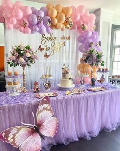 a purple table topped with lots of balloons and cake next to a giant pink butterfly