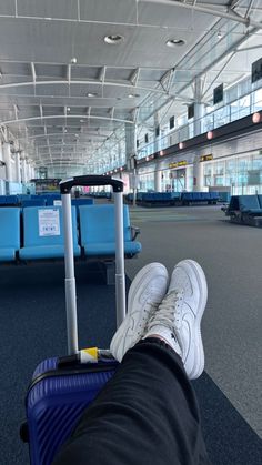 a person's feet resting on a piece of luggage in an airport with blue seats