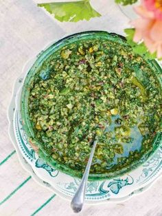 a bowl filled with pesto on top of a white and blue plate next to flowers