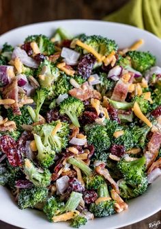 a white bowl filled with broccoli and cranberry salad on top of a wooden table