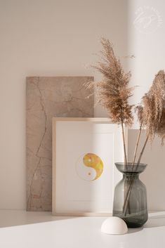 a vase with some dried plants in it next to a framed photograph and an egg