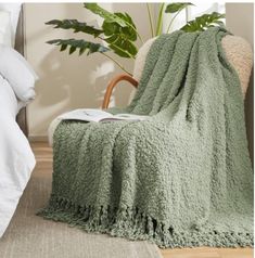 a green blanket sitting on top of a bed next to a chair and potted plant