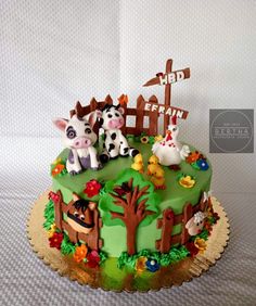 a birthday cake decorated with farm animals on top of a green field and wooden fence