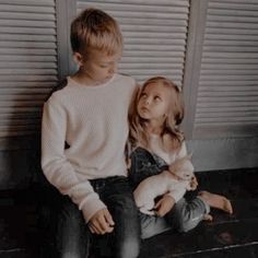 two young children sitting on the floor next to each other with one holding a dog