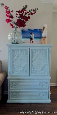 a blue cabinet with flowers in a vase on top of it next to a couch