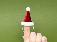 a finger pointing at a santa hat on top of a green background with white string