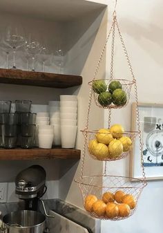 hanging fruit basket in the kitchen filled with oranges and cucumbers, next to a coffee maker