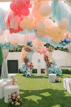 an outdoor ceremony with balloons and flowers on the grass, decorated in pastel colors