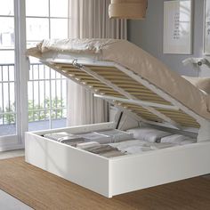 an open white bed frame sitting on top of a wooden floor next to a window