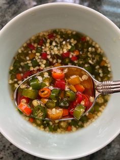 a white bowl filled with soup on top of a marble counter next to a metal spoon