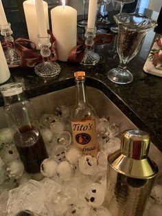 an empty bottle sitting on top of ice in a sink next to candles and glasses