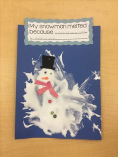 a snowman made out of paper on top of a wooden table next to a blue book