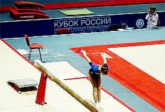 a woman is doing an acrobatic trick on the balance beam in a competition