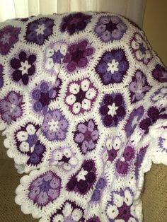 a purple and white crocheted blanket sitting on top of a couch next to a window